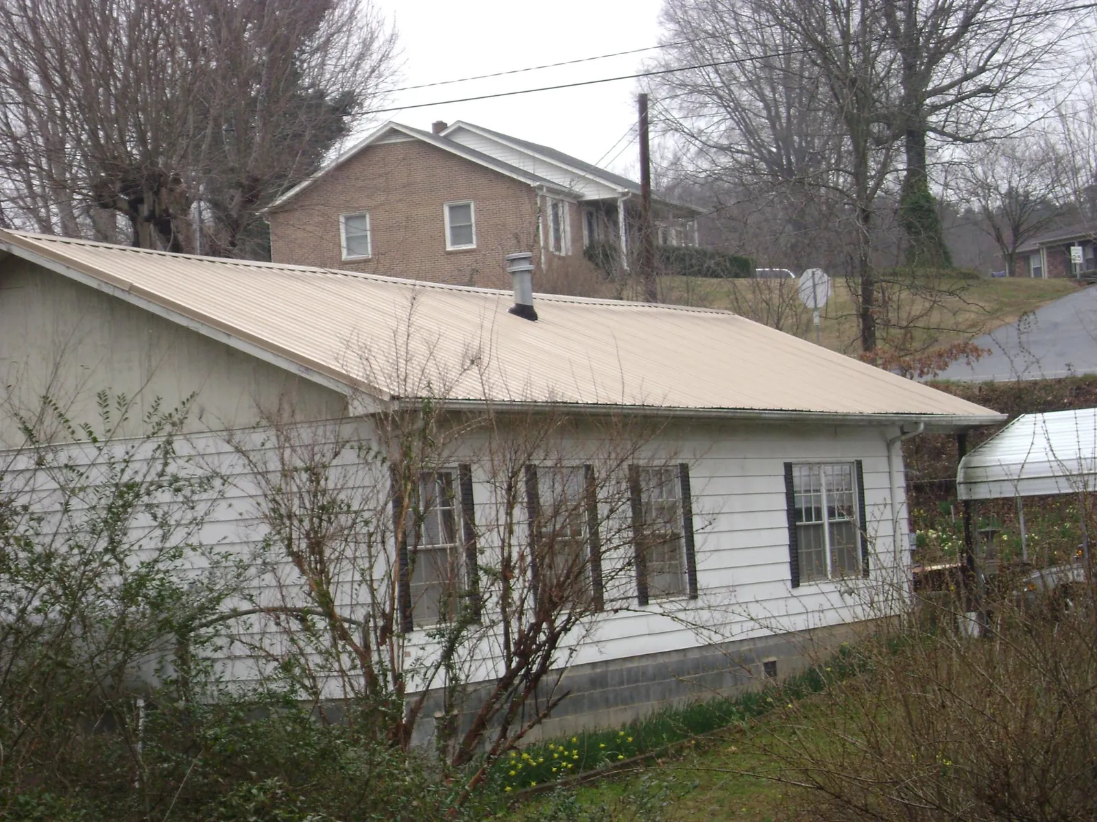 Tan metal roof on a white sided house set into a hillside — Commercial Roofing by Roofing Brothers in Grantsville